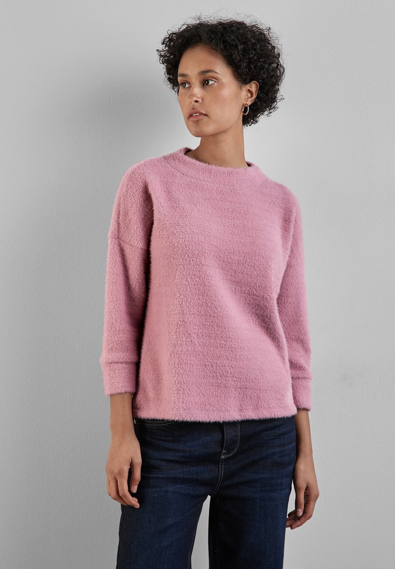 Helles rosa Sweatshirt mit einer weichen, strukturierten Oberfläche, Rundhalsausschnitt und 3/4-Ärmeln, kombiniert mit dunkelblauen Jeans.