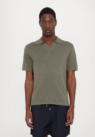 Olive green short-sleeve polo shirt with a v-neck, featuring a textured knit fabric and a straight hem. Worn with navy shorts.