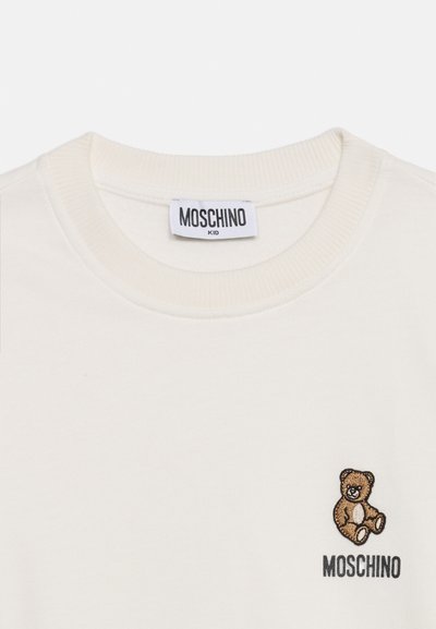 Λευκό παιδικό πουκάμισο Moschino με στρογγυλή λαιμόκοψη, με μικρή καφέ αρκούδα και κεντημένο λογότυπο Moschino στο στήθος.