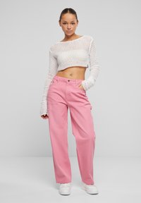 Bijeli mrežasti crop top i ružičaste široke hlače, s gumbima i bočnim džepovima, uparen s bijelim tenisicama. Cjelokupna tkanina je glatka.