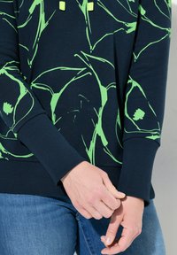 Marineblauwe sweatshirt met levendige groene abstracte patronen, voorzien van een geribde zoom en manchetten. Inclusief capuchon met contrasterende groene trekkoorden.