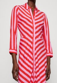 Abito camicia a righe rosse e rosa con bottoni sul davanti, colletto e maniche tre quarti, realizzato in un tessuto leggero e texture.