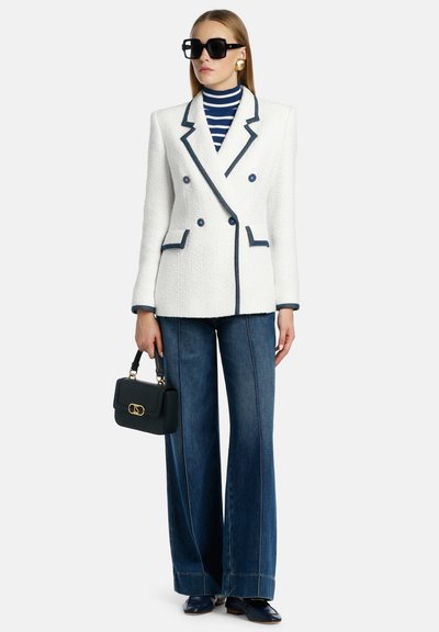 Witte tweed dubbelbreasted blazer met marineblauwe piping, gecombineerd met blauwe wide-leg jeans. Zwart handtasje en oversized zwarte zonnebril.