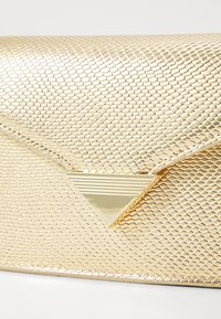 Clutch bag in tessuto dorato con motivo a pelle di serpente, dotata di un fermo triangolare dorato con linee orizzontali. Design compatto e rettangolare.