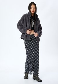 Veste grise et duveteuse sur un top noir court, associée à une longue jupe à carreaux en marine, crème et jaune, complétée par des bottines noires.