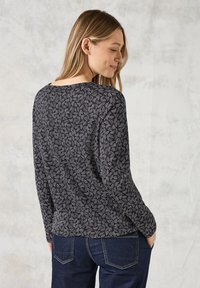 Haut à manches longues en noir avec un motif de feuilles abstrait blanc, encolure ronde, tissu doux et coupe décontractée. Associé à un pantalon en denim foncé.