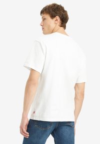 Weißes Baumwoll-T-Shirt mit Rundhals, kurzen Ärmeln und einem kleinen Markenlabel am Saum, kombiniert mit blauen Jeans.