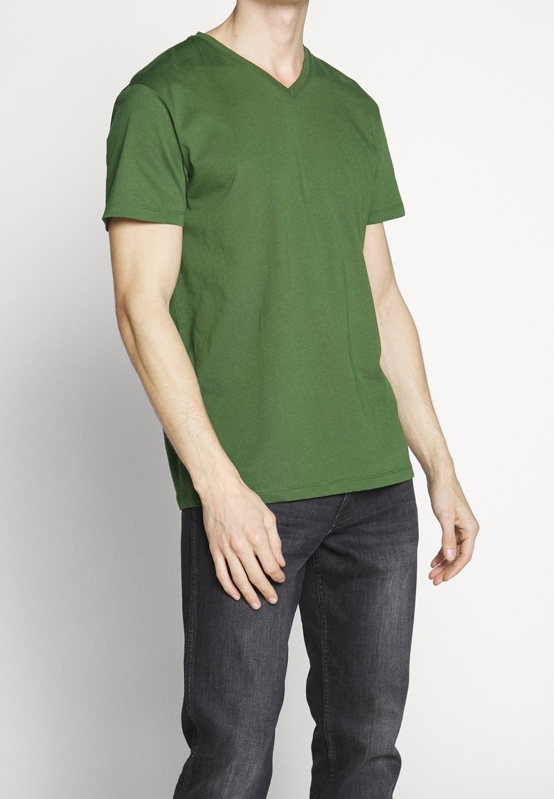 Grön bomulls t-shirt med v-hals, korta ärmar och avslappnad passform. Buren med mörka jeans, vilket visar en jämn och slät textur.