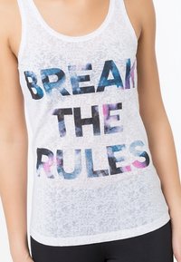 Camiseta sin mangas blanca con tela texturizada, con un llamativo gráfico de letras multicolores que dice "ROMPE LAS REGLAS" en el frente.