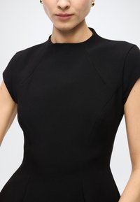 Black fitted dress with cap sleeves, high neckline, and dart seams. Smooth texture with structured silhouette. No visible patterns or accents.