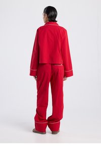 Punavalkoraidallinen pyjama, jossa on lyhyt takki ja väljät housut. Hihansuissa ja housujen helmassa valkoiset somisteet. Pehmeä materiaali, rento malli.