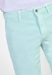 Licht mintgroene katoenbroek met een gladde textuur, voorzien van een gulp aan de voorkant, riemlussen en een zilveren knoop bij de tailleband.