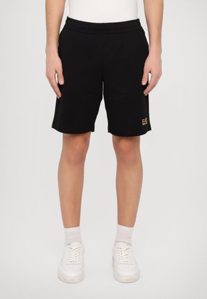 Crne kratke hlače napravljene od mekog materijala, s elastičnim pojasom, bočnim džepovima i zlatnim EA logotipom na lijevoj nozi.