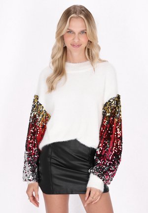 Maglione bianco peloso con maniche sovradimensionate in paillettes rosse, dorate e argentate; abbinato a una mini gonna nera in pelle.