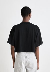 Černé zkrácené tričko vyrobené z bavlny, s krátkými rukávy a kulatým výstřihem, kombinované se světlými šedými džíny s vysokým pasem.