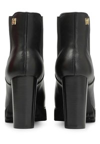 Mustade nahast pahkluu saapad plokk-kontsad, tagantvaade, väikese kuldse metallist logoga detailiga ülaääre lähedal.