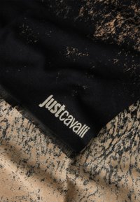 Bufanda negra y beige con un patrón texturizado, que presenta un prominente logo blanco "justcavalli" en uno de los bordes. Tela suave con bordes con flecos.