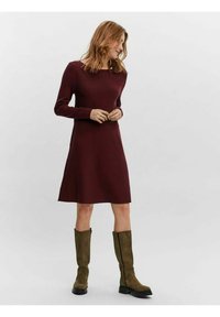 Abito bordeaux a maniche lunghe con silhouette dritta, realizzato in materiale knit. Abbinato a stivali al ginocchio verde oliva.