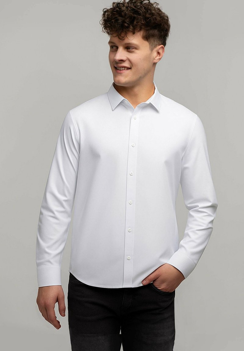 Biała koszula z długim rękawem, z wywinietym kołnierzykiem, z przodu zapinana na guziki, wykonana z gładkiego materiału; w połączeniu z ciemnymi spodniami, widoczny subtelny detal na nadgarstku.