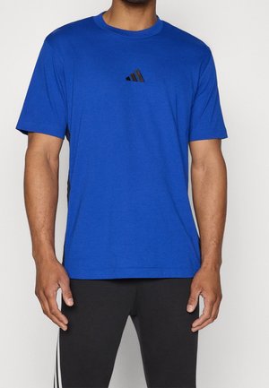 Homme portant un t-shirt Adidas bleu avec un logo noir, associé à un pantalon noir avec des bandes blanches sur les côtés.
