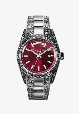 Montre en argent avec des motifs gravés ornementaux, un cadran rouge, affichage du jour et de la date, et logo Thomas Sabo sur le cadran.