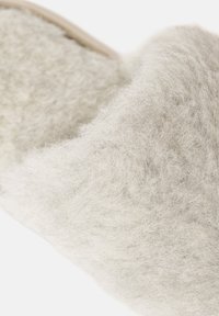 Hellgraue Filzpantoffel mit einer weichen, texturierten Oberfläche, die eine geschwungene Form und ein minimalistisches Design aufweist. Akzentuiert mit einer naturfarbenen Lederbesatz.