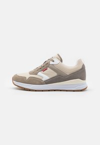 Sneaker beige e grigio con una combinazione di suede e pelle liscia, con dettagli bianchi e suola in gomma. Inclusi lacci e un dettaglio del logo.
