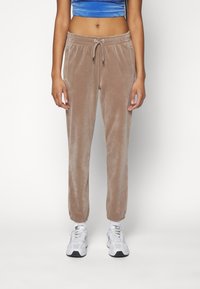 Velvet joggers in lichtbruin met een trekkoord in de taille, zijzakken en elastische manchetten, gecombineerd met witte sportschoenen.