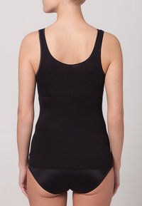 Svart ärmlös topp med en rundad ryggdesign, tillverkad av ett mjukt tyg, figurnära snitt och minimala sömmar för ett sömlöst utseende.