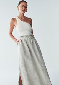 One-shoulder ribbed white top paired with a light gray linen maxi skirt featuring a gathered waistband and a side slit.