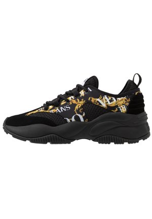 Zapatilla deportiva negra con parte superior de tela estampada con detalles dorados, paneles texturizados y una suela de goma negra texturizada.