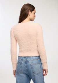 Maglione morbido rosa chiaro con maniche lunghe, aderente in vita, indossato con jeans di denim blu a vita alta, dotati di tasche posteriori.