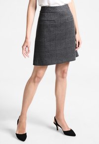 Mini jupe en tartan gris en tissu texturé, dotée de deux poches avant et d'un ourlet évasé. Portée avec des chaussures à talons noirs.