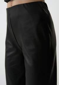Zwarte leren broek met een gladde textuur en een hoge taille. Heeft een schoon ontwerp en subtiele stiksels langs de naden.