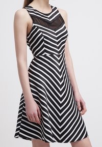 Svart och vit randig klänning med figursydd bodice och utsvängd kjol, med en genomskinlig panel vid halsringningen och ett zigzag-mönster.