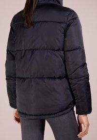 Puffjacka i mörk marinblå, med ett kviltat mönster och horisontella sömmar, hög krage och len satinliknande textur.