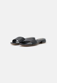 Sandalias de tiras abiertas negras con un upper de cuero suave, diseño de tiras cruzadas amplias y un tacón bajo tipo bloque. Plantilla texturizada para mayor comodidad.