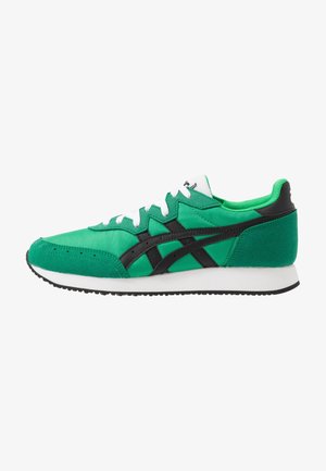 Baskets de sport vertes avec des rayures noires, des lacets blancs et une semelle intermédiaire blanche, présentées de profil sur fond blanc.