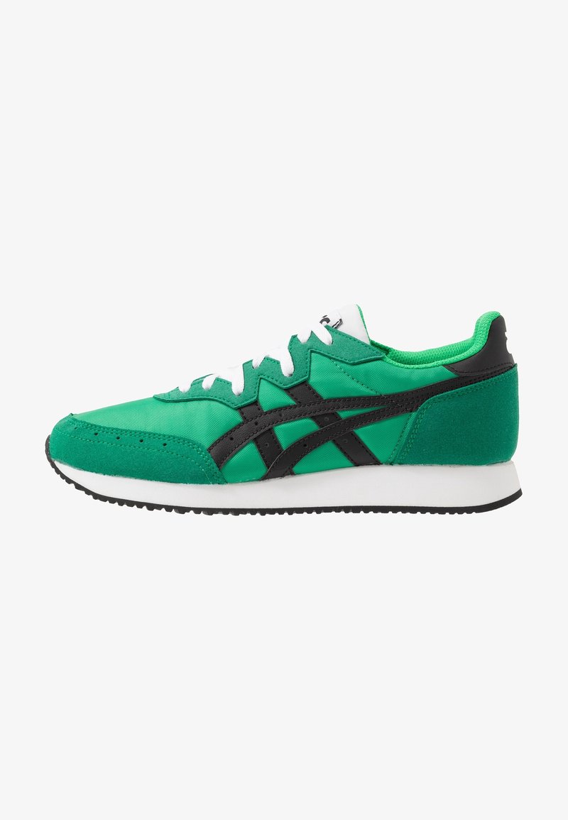 Baskets de sport vertes avec des rayures noires, des lacets blancs et une semelle intermédiaire blanche, présentées de profil sur fond blanc.