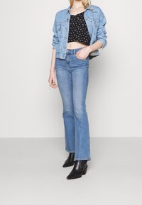 Džínová bunda ve světle modré, černý květinový crop top, vysoké modré džíny s mírným rozšířením, doplněné černými lodičkami na kotníku.
