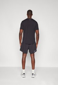 Camiseta deportiva negra y pantalones cortos, con una textura suave y un logo en la pierna izquierda. Se lleva con calcetines y zapatillas deportivas blancas.