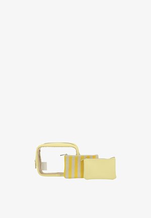 Tre borsette da bagno gialle: una trasparente con cerniera, una piccola a righe, una tinta unita, disposte fianco a fianco su sfondo bianco.