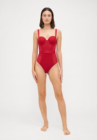Roter Einteiler-Badeanzug mit formenden Cups, breiten Trägern und hohem Beinausschnitt. Glatte Textur mit taillierter Passform und Netzdetails.