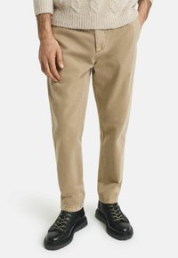 Pantalones de algodón beige de corte recto, con un diseño clásico. Combinados con botas negras de cordones y un suéter de punto color crema.