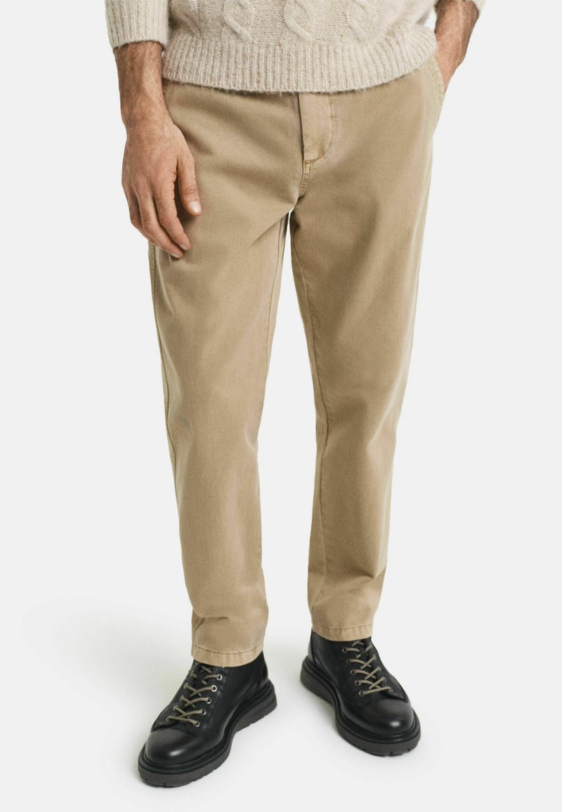 Pantalones de algodón beige de corte recto, con un diseño clásico. Combinados con botas negras de cordones y un suéter de punto color crema.