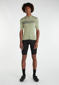Cyklistický dres s krátkym rukávom v svetlo zelenej farbe s čiernymi horizontálnymi pruhmi, v kombinácii s čiernymi šortkami s vypchávkami a čiernymi cyklistickými topánkami.