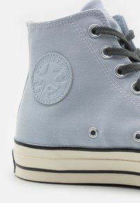 Světle modré plátěné sneakersy typu high-top se šedými tkaničkami, gumovou podrážkou, bílou mezipodešví a kulatou nášivkou s hvězdným designem.