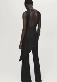 Vestido negro sin mangas con un dobladillo triangular y asimétrico, espalda descubierta con cierre de lazo y textura suave. Diseñado para una silueta ajustada.
