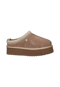 Mule en daim marron à plateforme et sans lacet avec un bord tressé et une petite étiquette en métal sur le côté, présenté sur un fond blanc.