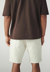 Tenue masculine composée d'une chemise en coton marron et d'un short en denim vert clair avec un ourlet retroussé et deux poches arrière.